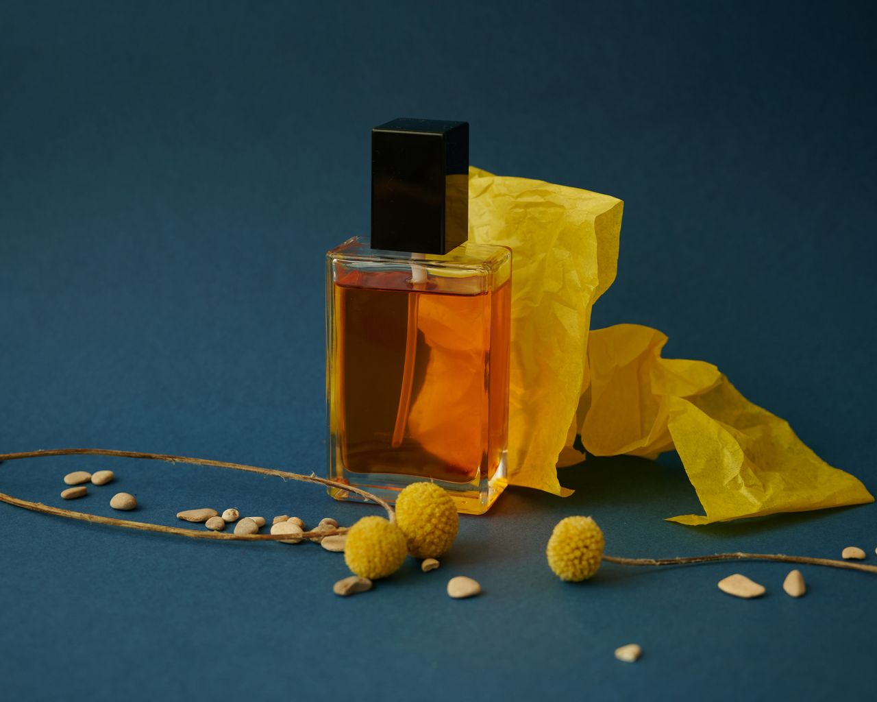 Modern still life featuring a glass perfume bottle with yellow paper and floral accents, offering a vibrant touch.